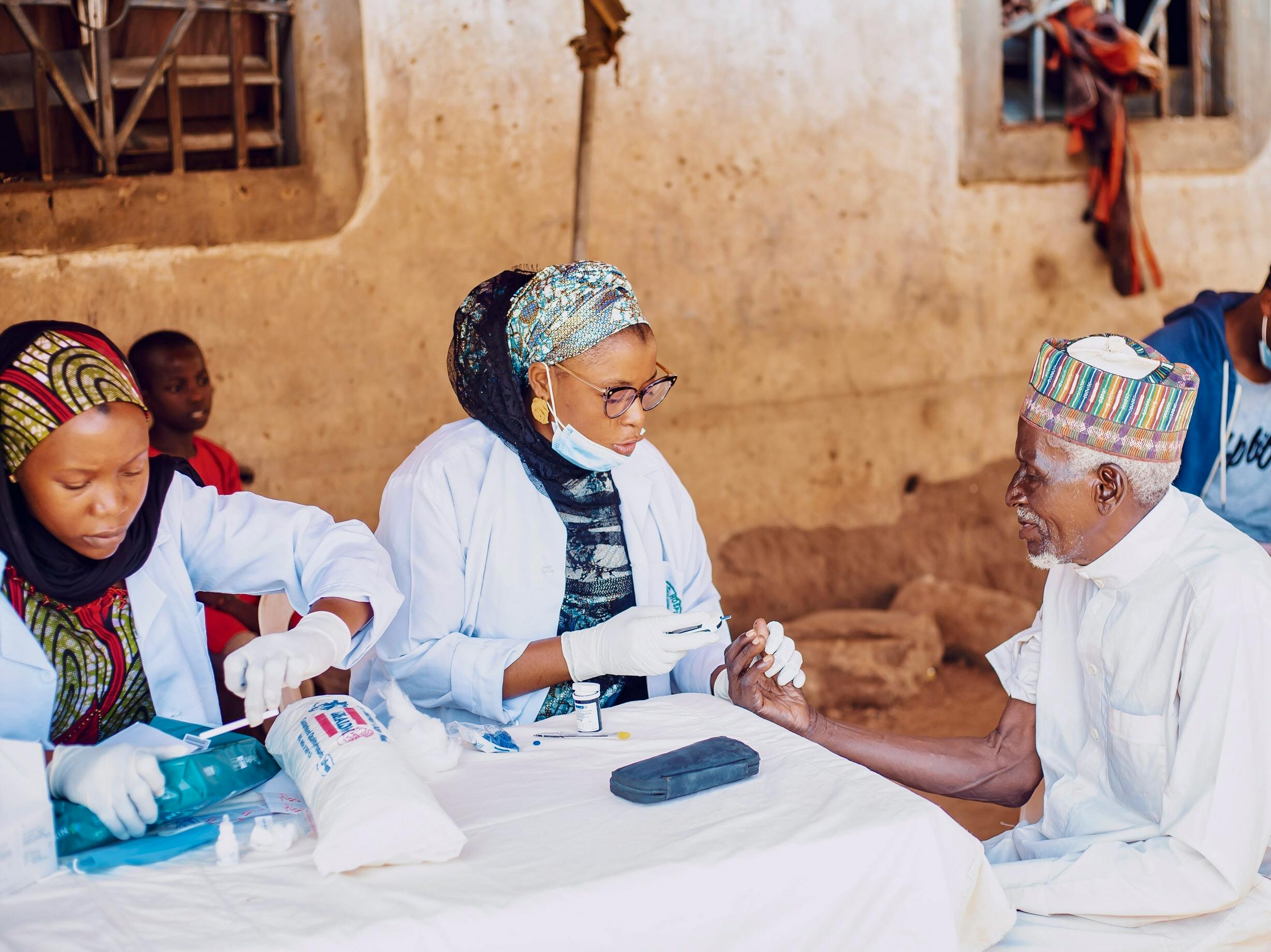 Healthcare workers assisting elderly man during community outreach in Kaduna, Nigeria.